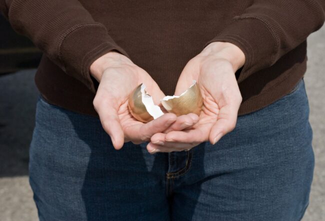 A person holding the broken halves of a golden egg shell in their hands.