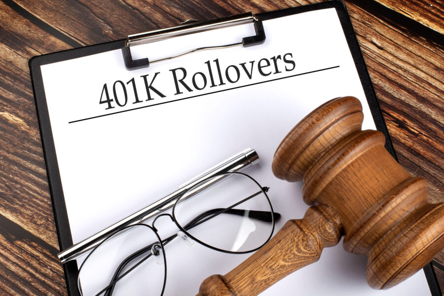 A clipboard titled "401K Rollovers" with a pair of glasses and a wooden gavel placed on a wooden surface, representing legal and financial concepts.