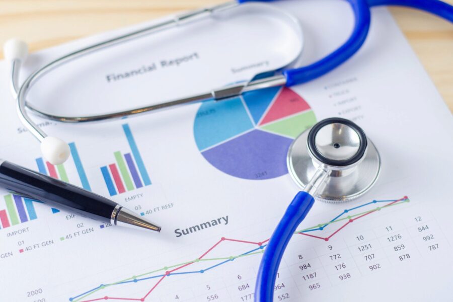 Stethoscope, pen, and financial report with graphs and charts, symbolizing the intersection of healthcare and financial analysis.