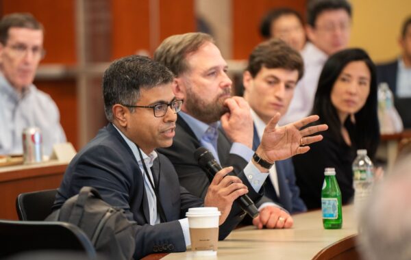 A group of people in a conference setting, one person speaking into a microphone while others listen attentively.