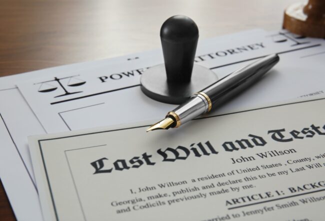 A last will and testament document alongside a power of attorney form with a fountain pen and a notary stamp on a wooden surface.