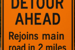 A road sign reading "Detour Ahead, Rejoins main road in 2 miles" on an orange background.